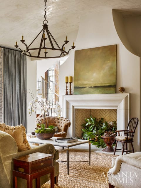Living room with a tufted brown sofa, green velvet armchair, marble-topped coffee table, and a fireplace with herringbone tile.