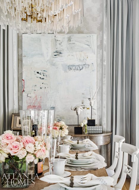 Dining room with a table set for a formal meal, featuring a large abstract painting, floral arrangements, and animal skull decor.