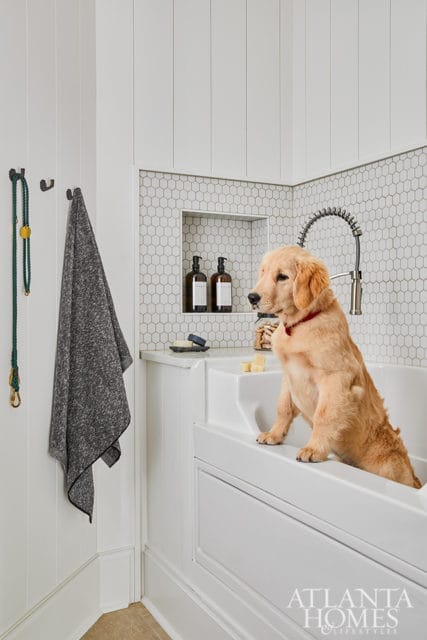 White dog bathing station with a golden retriever puppy sitting in the tub, hexagonal tile backsplash, and a gooseneck faucet.