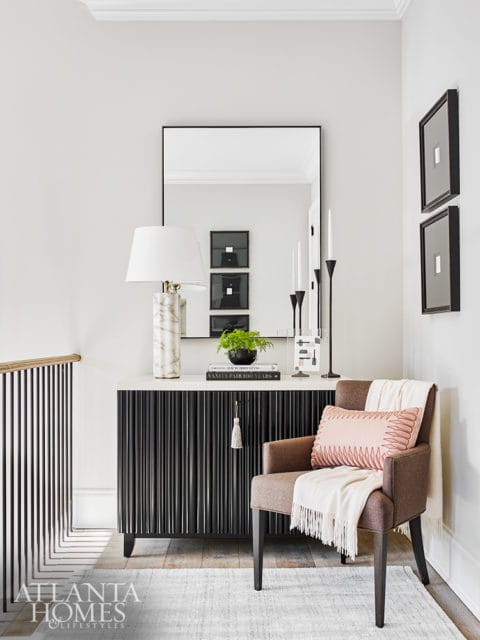 Hallway console with fluted black cabinet, marble lamp, and framed art. A brown armchair with pink and white throws sits nearby.