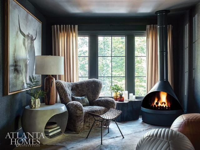 Dark living room with a black modern fireplace, textured armchair, large abstract art of a bull, and a concrete side table with a lamp.