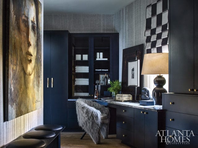 Dark blue built-in cabinetry with brass hardware, marble countertop, and a furry accent chair in a room with abstract art and a black and white checkered window treatment.