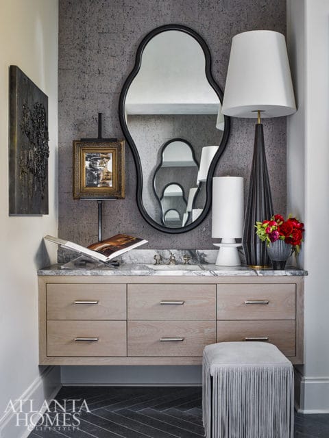 Floating light wood vanity with marble countertop and silver hardware, topped with a decorative mirror, lamps, and flowers.