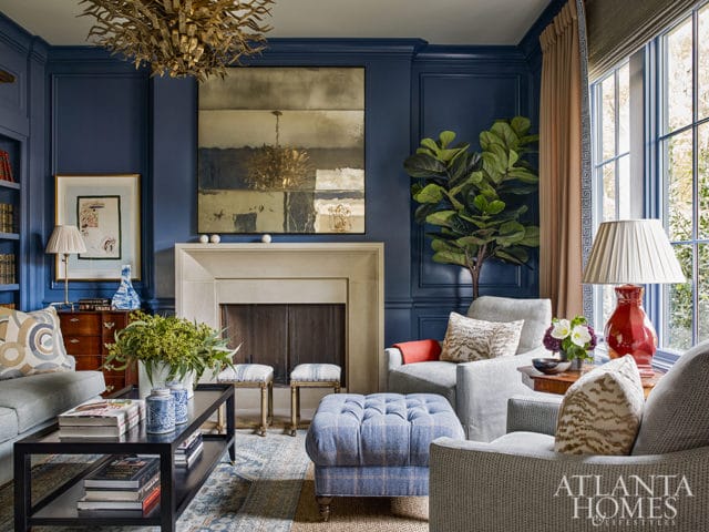 Living room with navy blue paneled walls, a cream fireplace, upholstered seating in gray and blue plaid, and a large abstract artwork above the mantel.