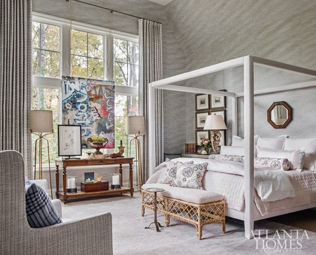 Gray textured wallpaper bedroom with a white canopy bed, pink bedding, rattan bench, and a console table with artwork and lamps.