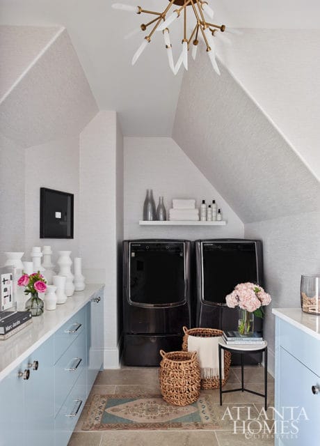 Laundry room with light gray textured wallpaper, light blue cabinets, two black washers, and a starburst chandelier.