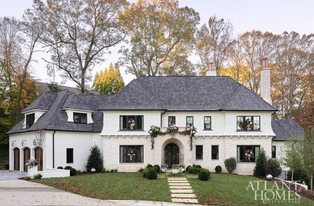 White and stone house with dark shingled roof, arched entryway, and festive holiday decorations.