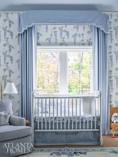 Nursery with white crib, blue floral bedding, wisteria wallpaper, and a striped armchair.