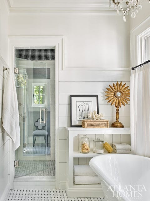 White bathroom with glass-enclosed shower, freestanding tub, shiplap walls, and decorative shelf with jars and sunburst mirror
