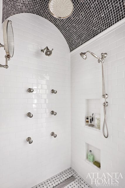 White subway tile shower with multiple chrome shower heads, arched ceiling with black and white mosaic tile, and marble-lined niches.