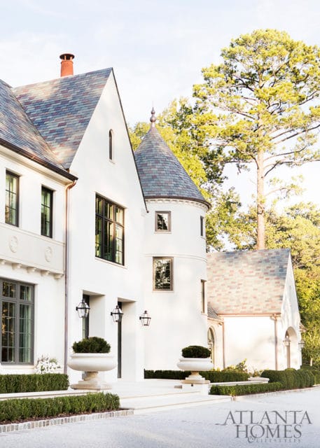White stucco mansion with a conical turret, slate roof, and formal landscaping. Atlanta Homes & Lifestyles logo in the lower right corner.