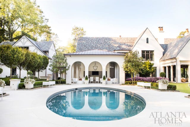 Luxury home with a circular pool, arched loggia with outdoor seating, manicured gardens, and white stucco exterior.