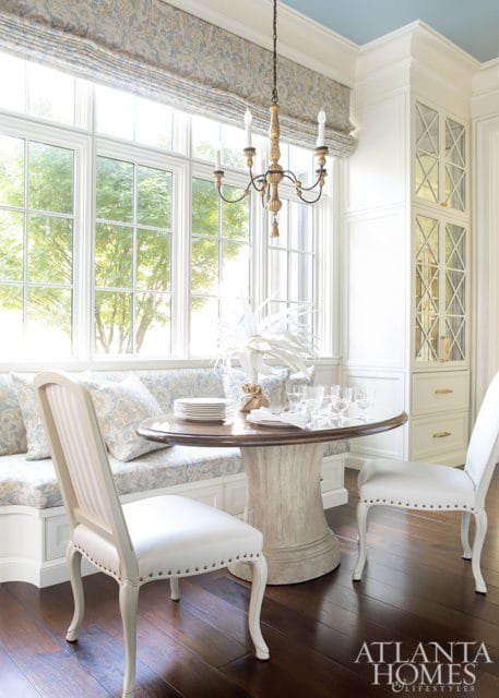 Breakfast nook with banquette seating upholstered in a blue and white floral fabric, round pedestal table set for dining, and two white upholstered chairs.