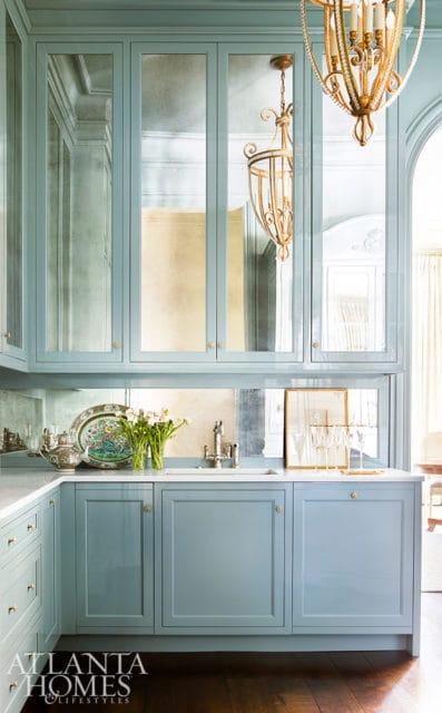 Light blue kitchen cabinetry with mirrored upper cabinet doors, white marble countertops, and a gold chandelier.