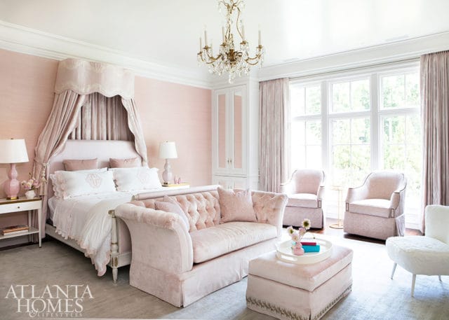 Pink upholstered bedroom with a canopy bed, tufted sofa, two armchairs, and a crystal chandelier.