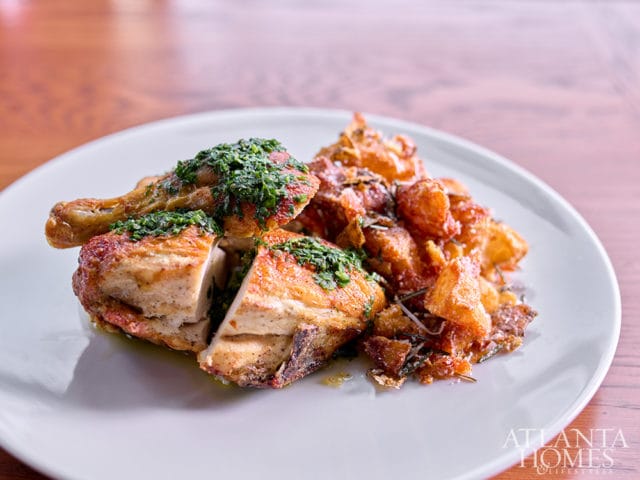 Roasted chicken pieces topped with green herb sauce served with crispy potatoes and rosemary on a white plate.