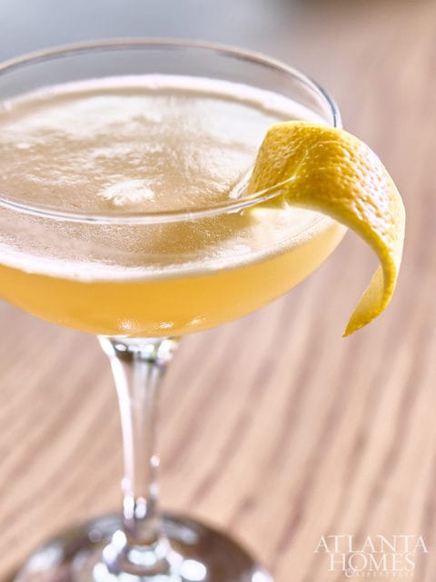 Close-up of a yellow cocktail in a coupe glass, garnished with a lemon twist.