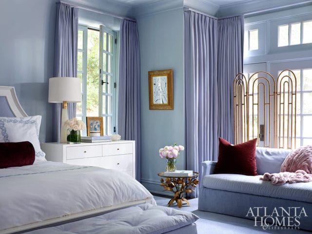 Light blue bedroom with a white dresser, a bed with white linens and a burgundy bolster pillow, and a blue chaise lounge with burgundy and pink pillows.