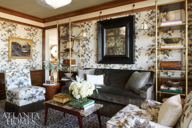 Living room with floral wallpaper, dark velvet sofa, patterned armchairs, marble-topped coffee table, and gold shelving unit.