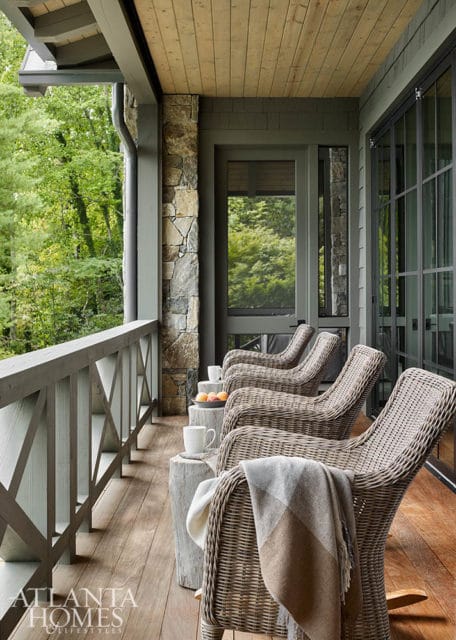 Covered porch with wicker chairs, wooden ceiling, stone accents, and large windows overlooking trees.