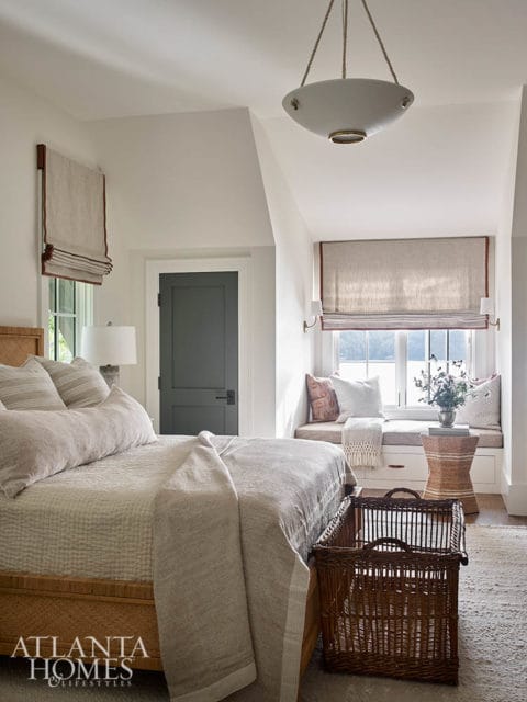 Bedroom with a light-colored bed, rattan headboard, woven baskets, and a window seat with cushions.
