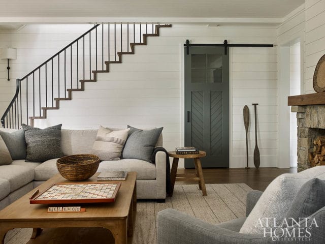 Living room with sectional sofa, wooden coffee table with Scrabble board, stone fireplace, and dark green barn door with glass panes.