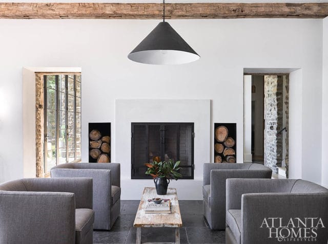 Living room with white fireplace, gray upholstered armchairs, rustic wood coffee table, and exposed wooden ceiling beam.