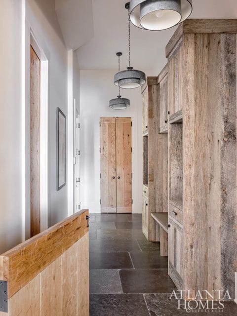 Hallway with slate tile flooring, rustic wood paneled walls and cabinetry, and three tiered pendant lights.