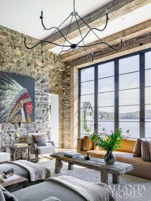 Living room with stone accent wall featuring Native American artwork, exposed wooden beams, and a large window overlooking a lake.