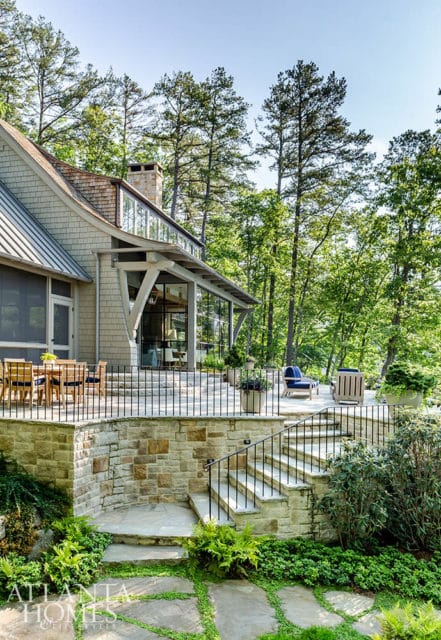 Stone patio with outdoor dining set and lounge chairs, leading to a multi-level stone staircase surrounded by lush greenery and tall trees.