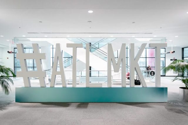 Large white 3D letters spelling #ATL MKT stand on a teal base in a modern lobby with escalators and plants in the background.