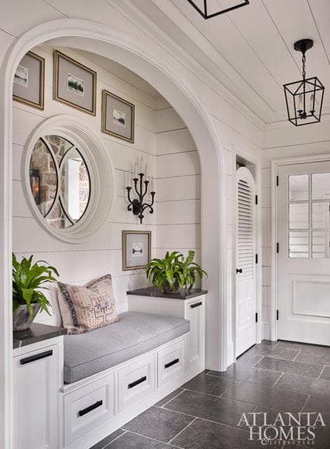Entryway with built-in white bench seating, shiplap walls, a round mirror, and a black geometric pendant light. Dark stone tile floor.