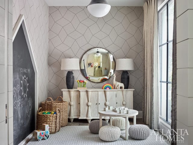 Playroom with geometric patterned wallpaper, a chalkboard wall, a distressed wood cabinet with lamps and toys, and a round coffee table with poufs.