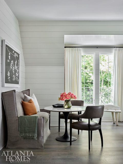 Dining area with shiplap walls, a gray upholstered banquette, marble-top tulip table, and leather chairs.