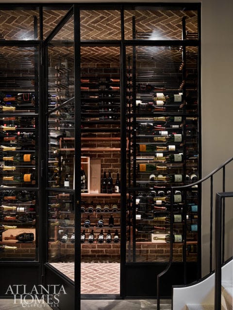 Glass-fronted wine cellar with brick walls and herringbone brick floor, filled with wine bottles on metal racks.