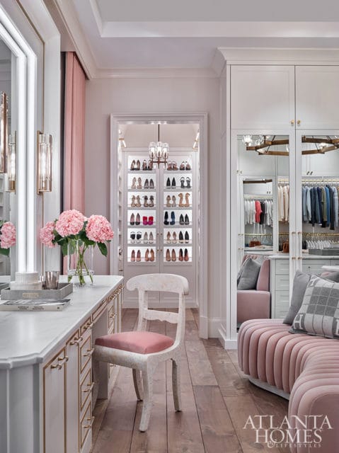 White closet with pink velvet seating, marble vanity, and illuminated shoe displays.