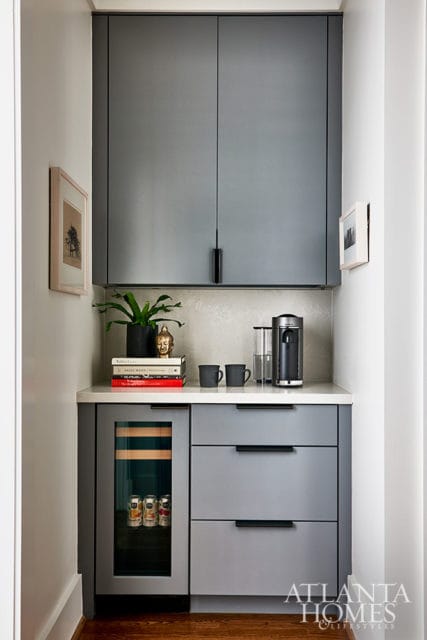 Gray built-in bar with a wine fridge, coffee maker, stacked books, and framed art on the wall.