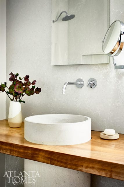 Modern bathroom with a concrete vessel sink on a wooden vanity, chrome wall-mounted faucet, and a large mirror reflecting a shower head.