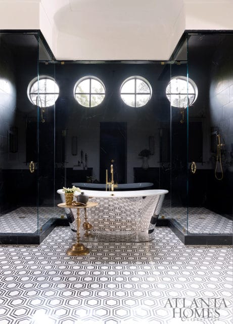 Modern black bathroom with a freestanding silver tub, glass-enclosed showers, and geometric black and white floor tiles.