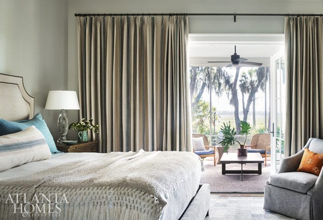 Bedroom with upholstered headboard, striped curtains, and a view of a covered patio with wicker chairs and a coffee table.