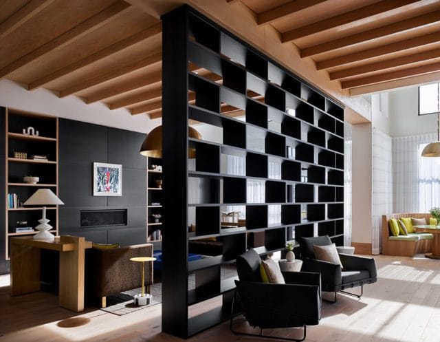 Living room with black open shelving room divider, dark gray armchairs, and built-in bookshelves flanking a fireplace. Wood plank ceiling and floors add warmth.
