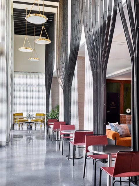 Lobby with red chairs and tables, yellow striped armchairs in the background, and decorative metal columns.
