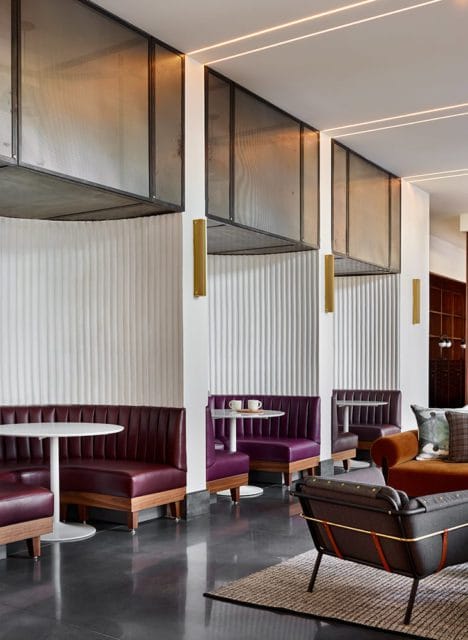 Modern lounge area with purple leather booths, white round tables, and dark gray seating. Textured white walls and metal grate ceiling panels add architectural interest.
