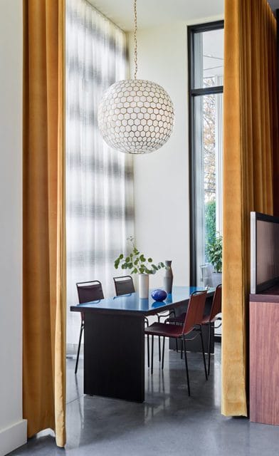 Dining room with a black table, maroon chairs, a large hexagonal pendant light, and gold velvet curtains.