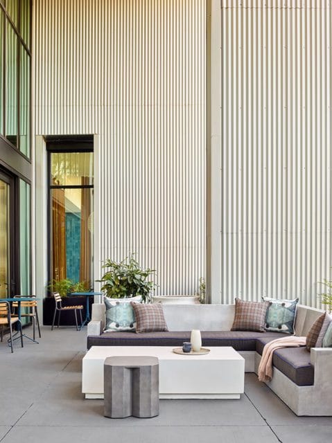 Modern sectional sofa with dark cushions and patterned throw pillows on a concrete patio, next to a white coffee table and a geometric side table.