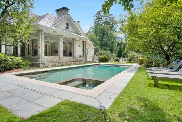 Luxury home with stone and white siding, covered porch with columns, and a rectangular swimming pool with a spa.