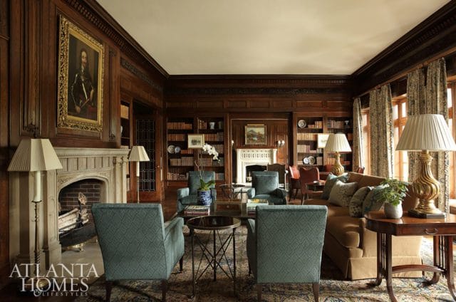 Library with dark wood paneling, stone fireplace, built-in bookshelves, and upholstered seating in teal and tan.
