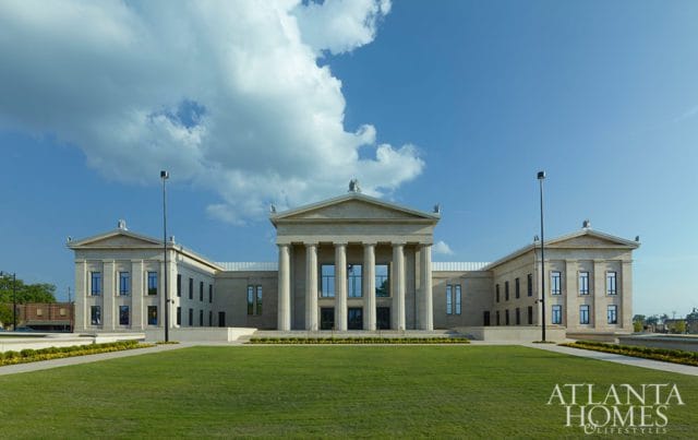 Neoclassical building with a central portico featuring tall columns, symmetrical wings, and a manicured lawn in front.