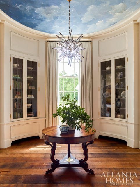 Dining room with a hand-painted sky ceiling, starburst chandelier, built-in glass-front cabinets, and a round wooden table