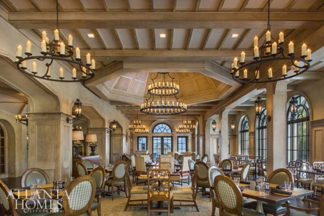 Elegant dining room with coffered wood ceilings, multiple wrought iron chandeliers with candle-style lights, and arched windows.